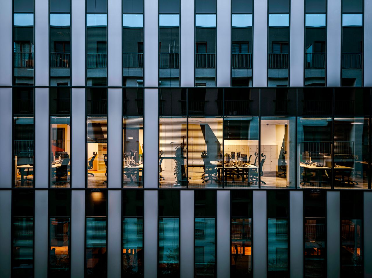 Oferta Illuminated office inside a modern glass building exterior, showcasing architecture and workspace design.