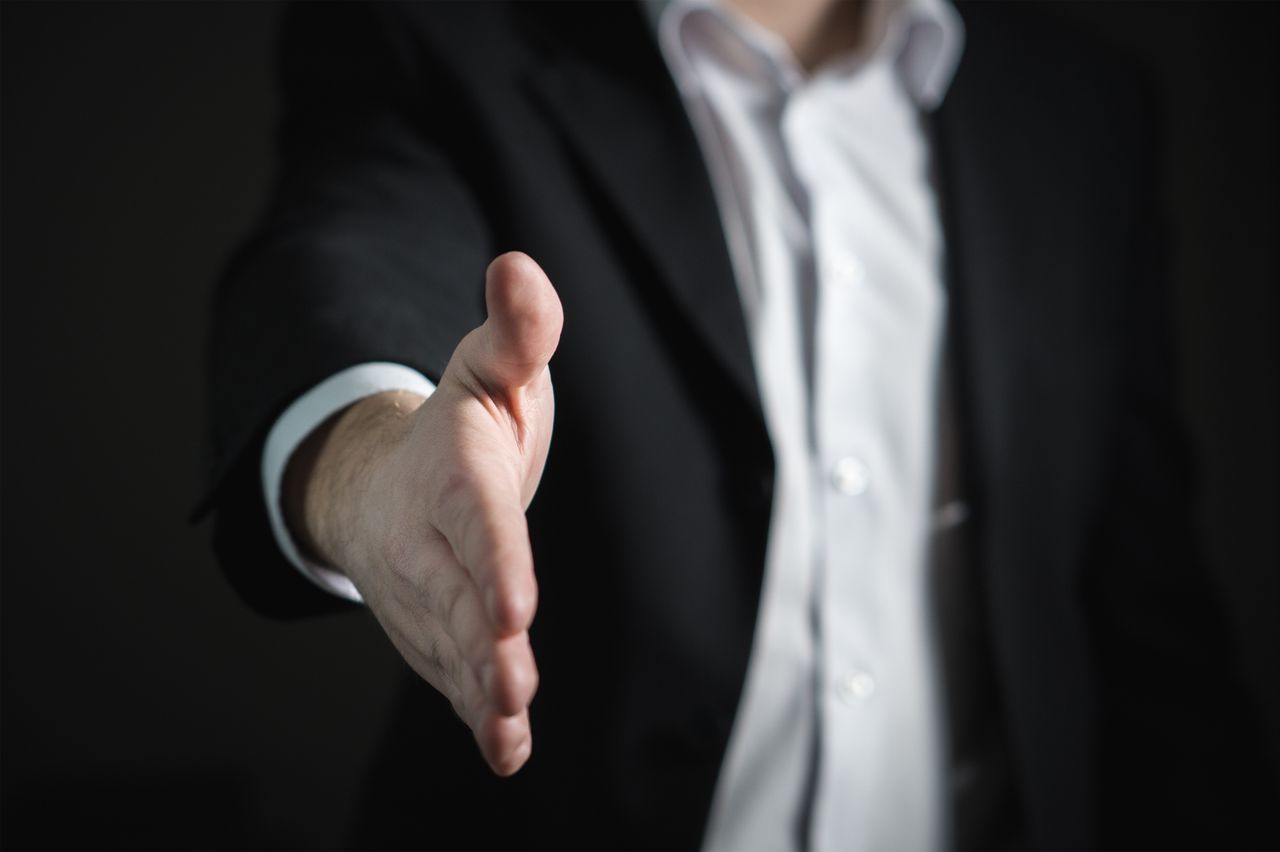 Strona główna Close-up of a businessman extending hand for a handshake, symbolizing agreement and partnership.