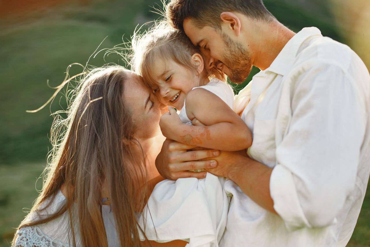 Strona główna A joyful family moment with parents embracing their child outdoors in warm sunlight.