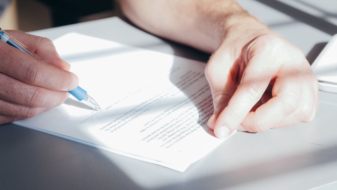 Strona główna Hands signing a contract with a blue pen, close-up view.